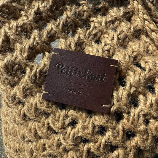 Dark brown leather label with text "PetiteKnit. Est. 2016"