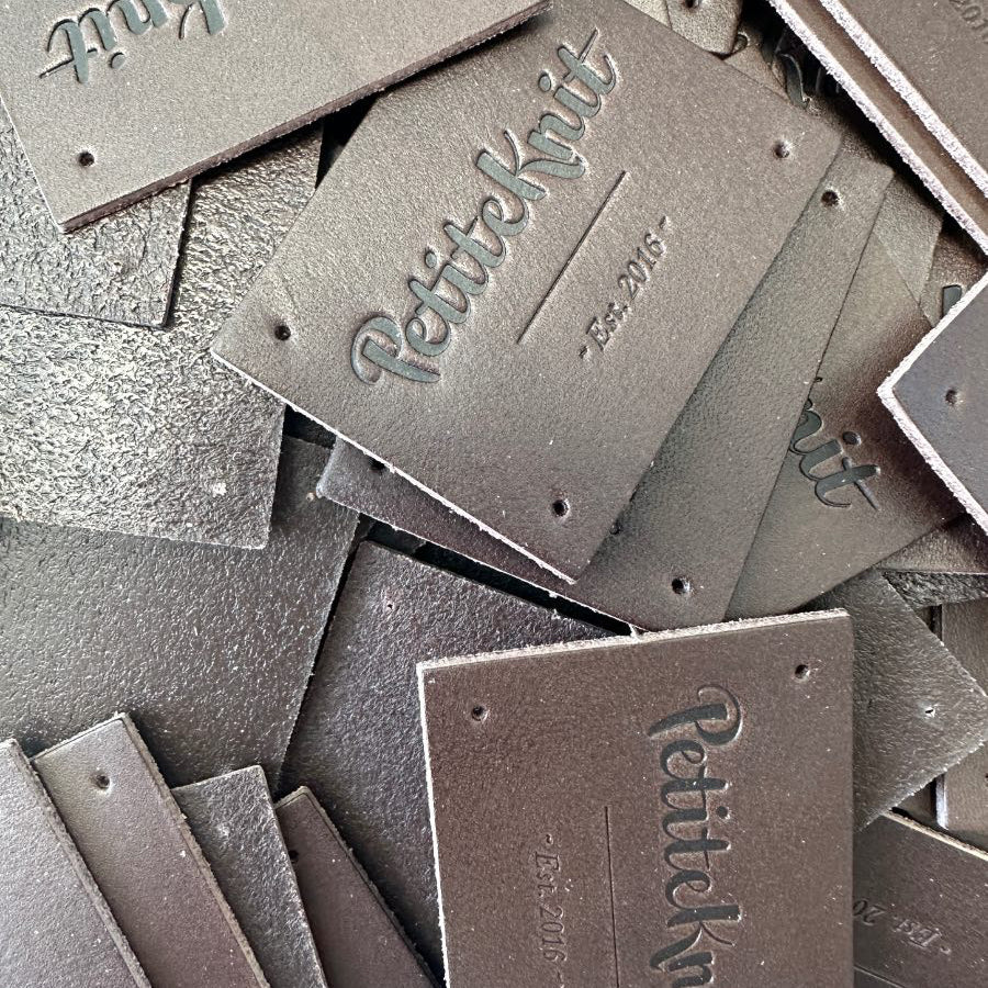 Dark brown leather label with text "PetiteKnit. Est. 2016"